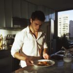 a young man stands by the counter with a small plate of food in front of him